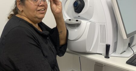 Lady sitting at eye check equipment while preparing to take off or put on a pair of spectacles.