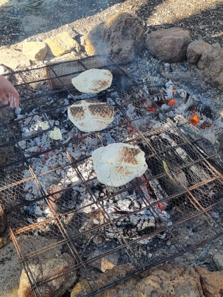 Flattened damper sitting on racks as it cooks above hot coals.