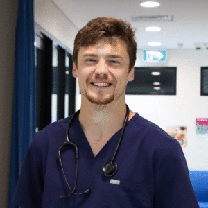 Man standing in a hallway looking at camera and wearing a stethoscope.